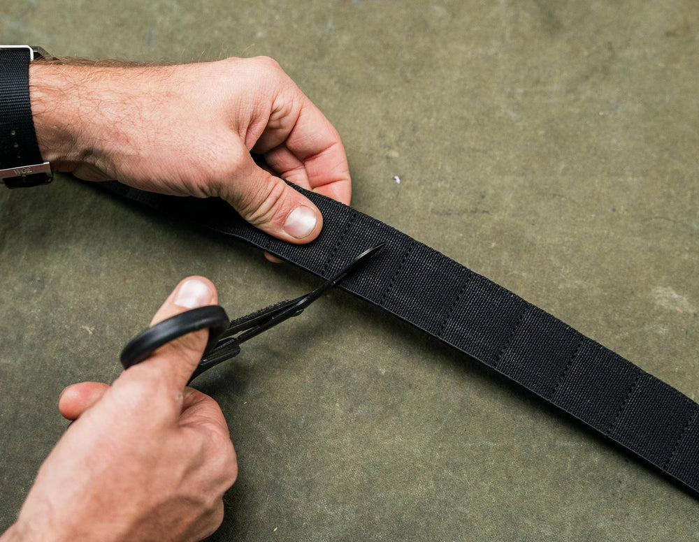 Every Day Belt in black woven nylon being trimmed to length with scissors, hands-on lifestyle shot on green surface
