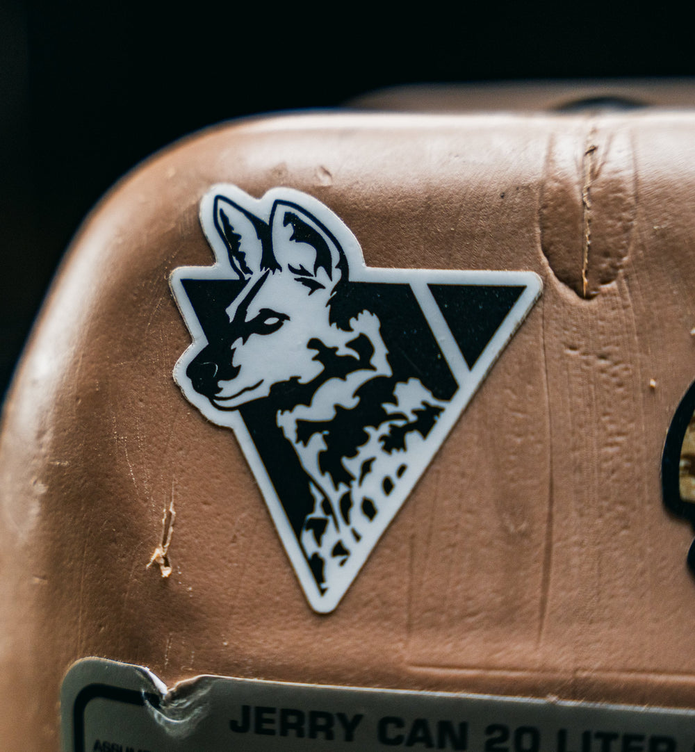 Dirty Civilian African painted dog die-cut sticker, black-and-white triangle logo, applied to a tan jerry can in close-up