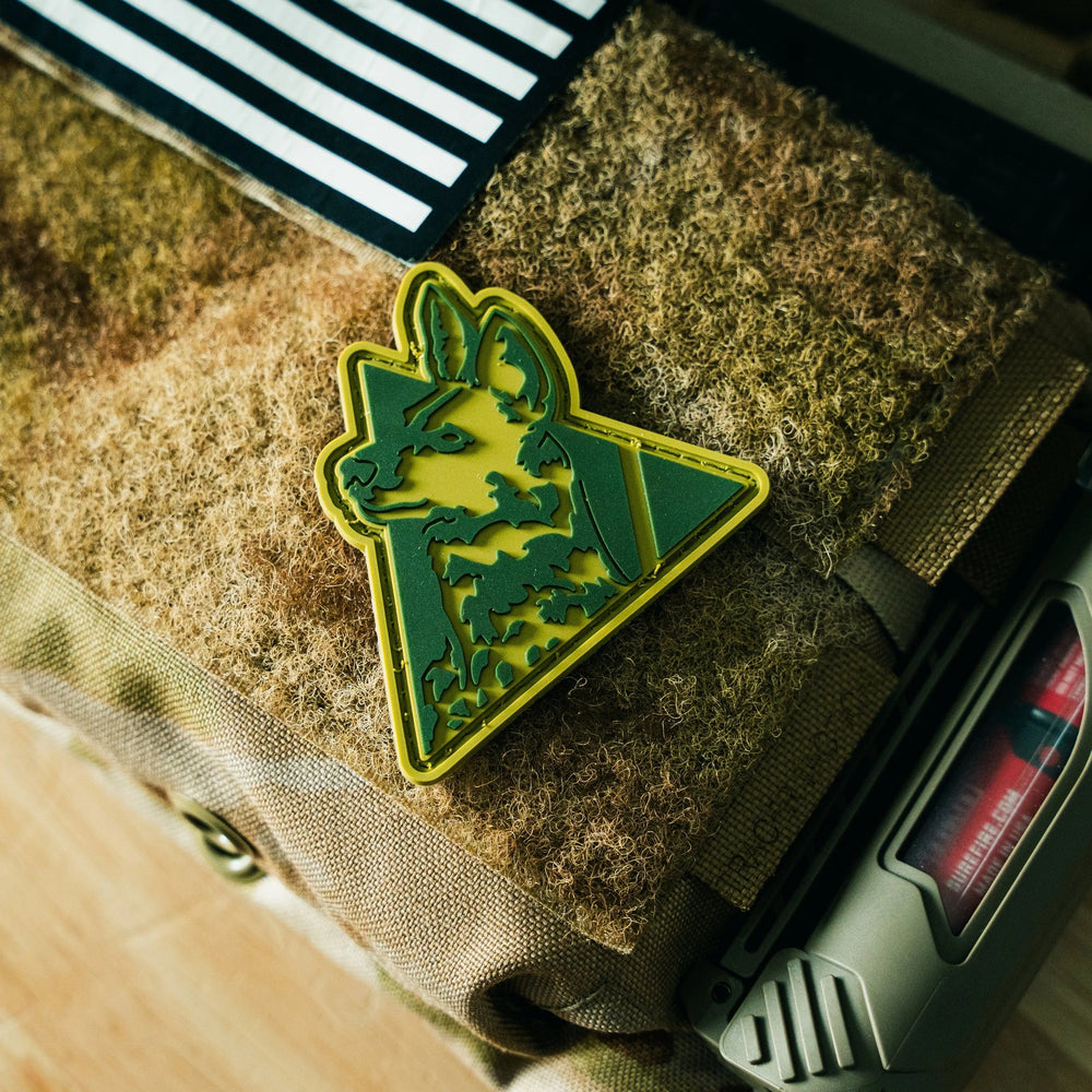 Dirty Civilian Logo Patch in olive and green PVC with dog-head triangle design, hook-backed, staged on tan velcro panel