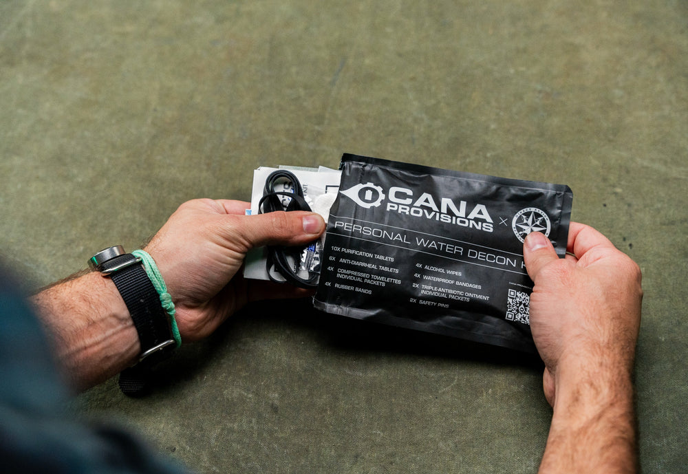 Hands opening the black CANA Provisions Personal Water Decon Kit pouch, contents label visible, over an olive backdrop