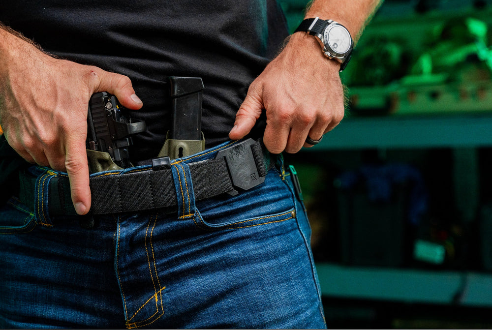 Every Day Belt worn on-body, black webbing strap and aluminum buckle on blue jeans holding an appendix-carry pistol