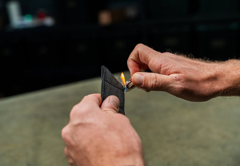Every Day Belt end held to a lighter flame, close-up durability test of the black woven nylon webbing