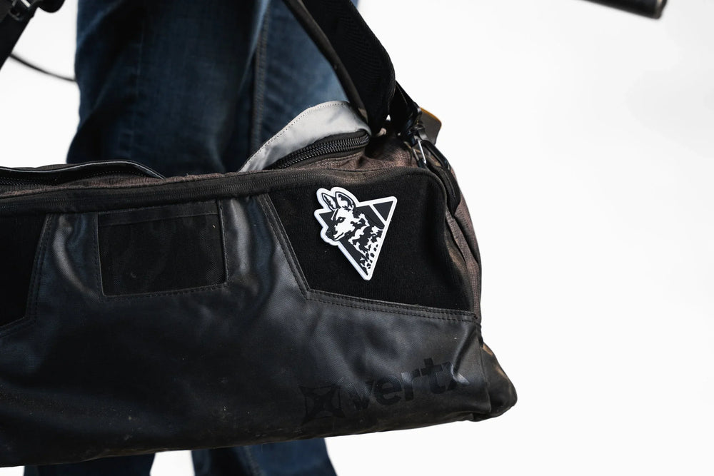 Dirty Civilian logo patch, black and white PVC wild dog head with triangle, velcro-mounted on a black duffel bag in use