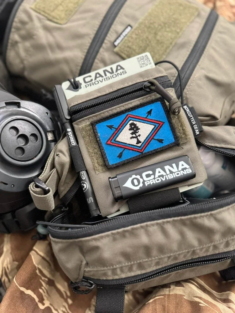 CANA MK Torch Pocket Lighter in black with CANA Provisions gear logo, staged on tan tactical gear in a lifestyle shot