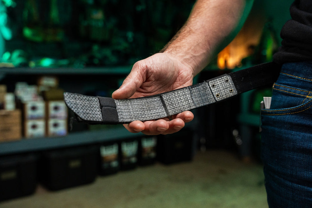 Agonic Every Day Belt in heathered gray woven fabric held across an open palm, showing brass rivets and black edging