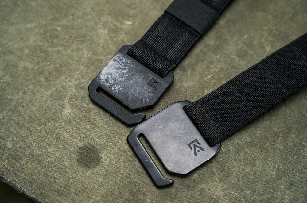 Agonic Every Day Belt close-up of two aluminum buckle finishes, black and raw gunmetal, with logo on black webbing